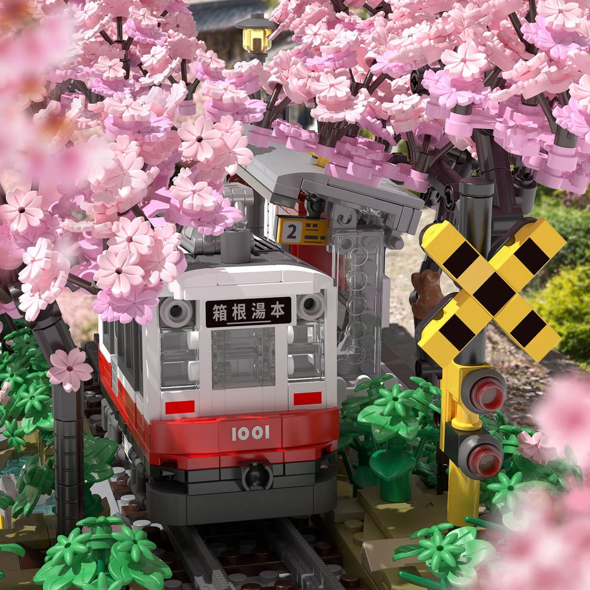 Model train set on tracks with cherry blossom trees and a crossing signal.